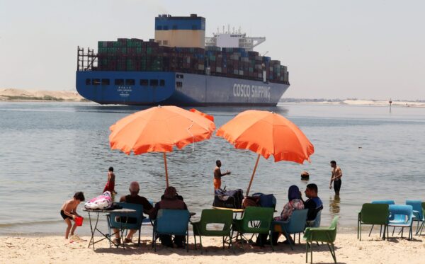 People swim in the Suez Canal as a container ship passes in Ismaila, Egypt, on May 27, 2021. © Khaled Elfiqi/EPA-EFE/Shutterstock