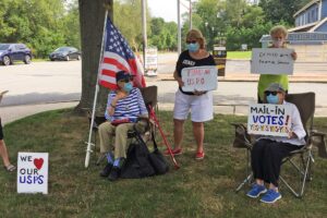 Author Catharine Stimpson and her wife Elizabeth Wood, both seated, demonstrate government cuts to the United States Postal Service at their local post office in Southold, NY, on August 22, 2020. Courtesy of Catharine Stimpson