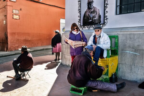 A man receives a shoeshine on a street corner, next to a man who is collecting spare change, in Potosi, Bolivia. © Tim Dirven/Panos/Redux