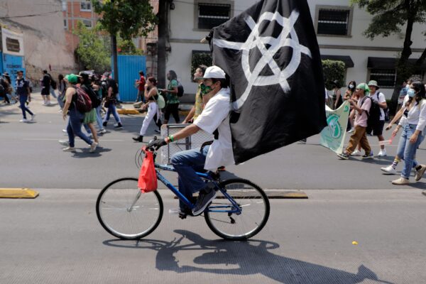 A man rides a bicycle while flying an Anarchist flag in Mexico City on April 20, 2023. © Gerardo Vieyra/NurPhoto/AP